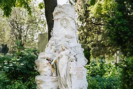 Marble tomb of Johann Strauss Sohn with his head in relief, plus a female figure, bat and an angel playing the violin in the towering monument.