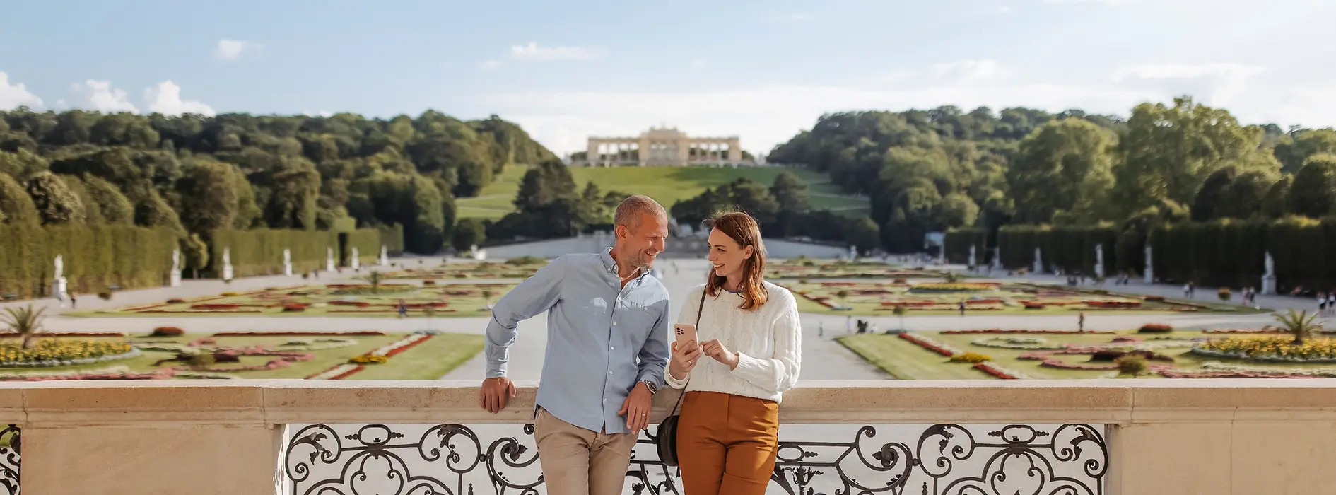 A couple looking at their cell phone together in the background: Schönbrunn Palace gardens and the Gloriette